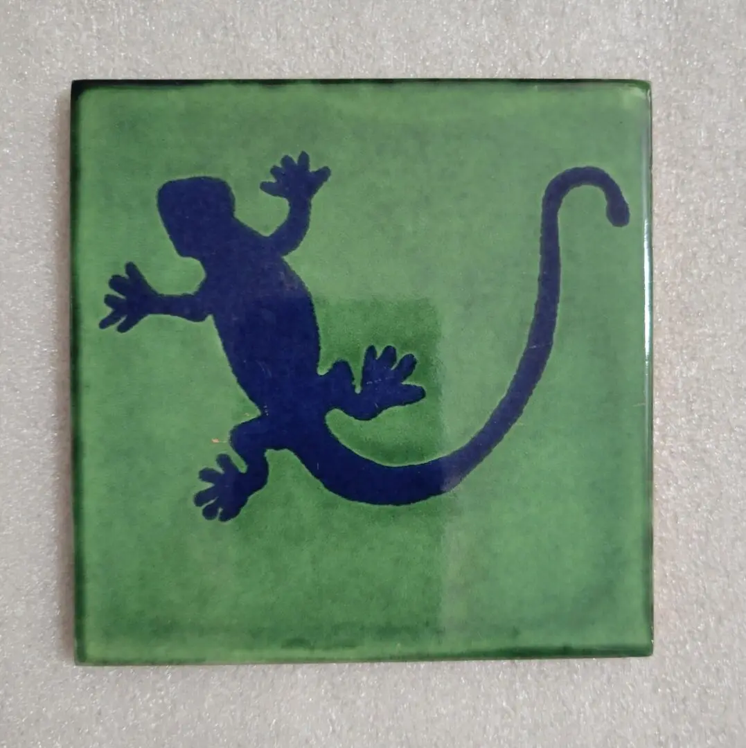 Blue gecko silhouette on a green square tile.