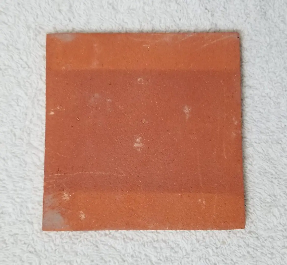 Weathered square terracotta tile on white towel