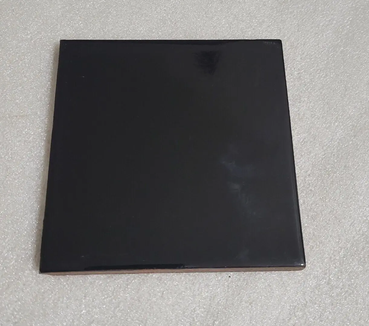 Black square ceramic tile on gray surface.