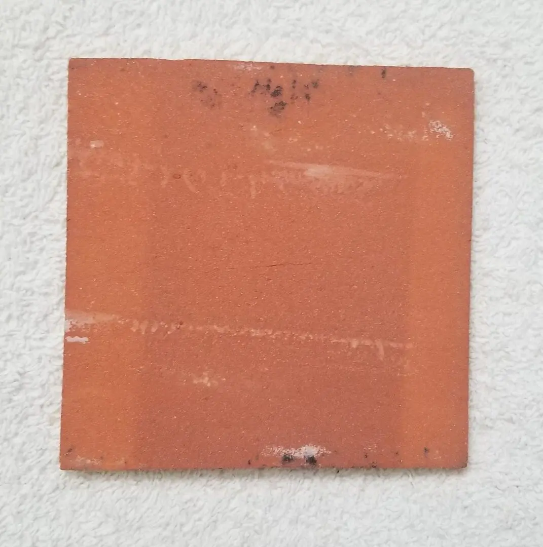 A single square terracotta tile with some markings on a white background.