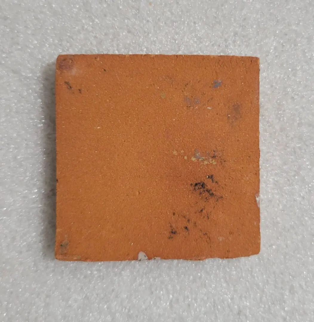 Worn square terracotta tile with scuffs