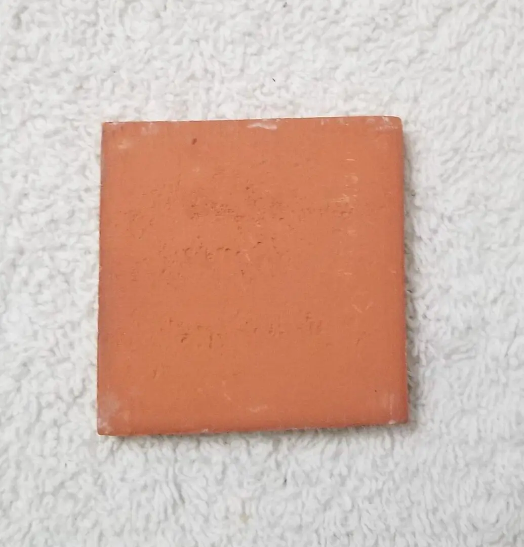 Terracotta square tile on textured surface.