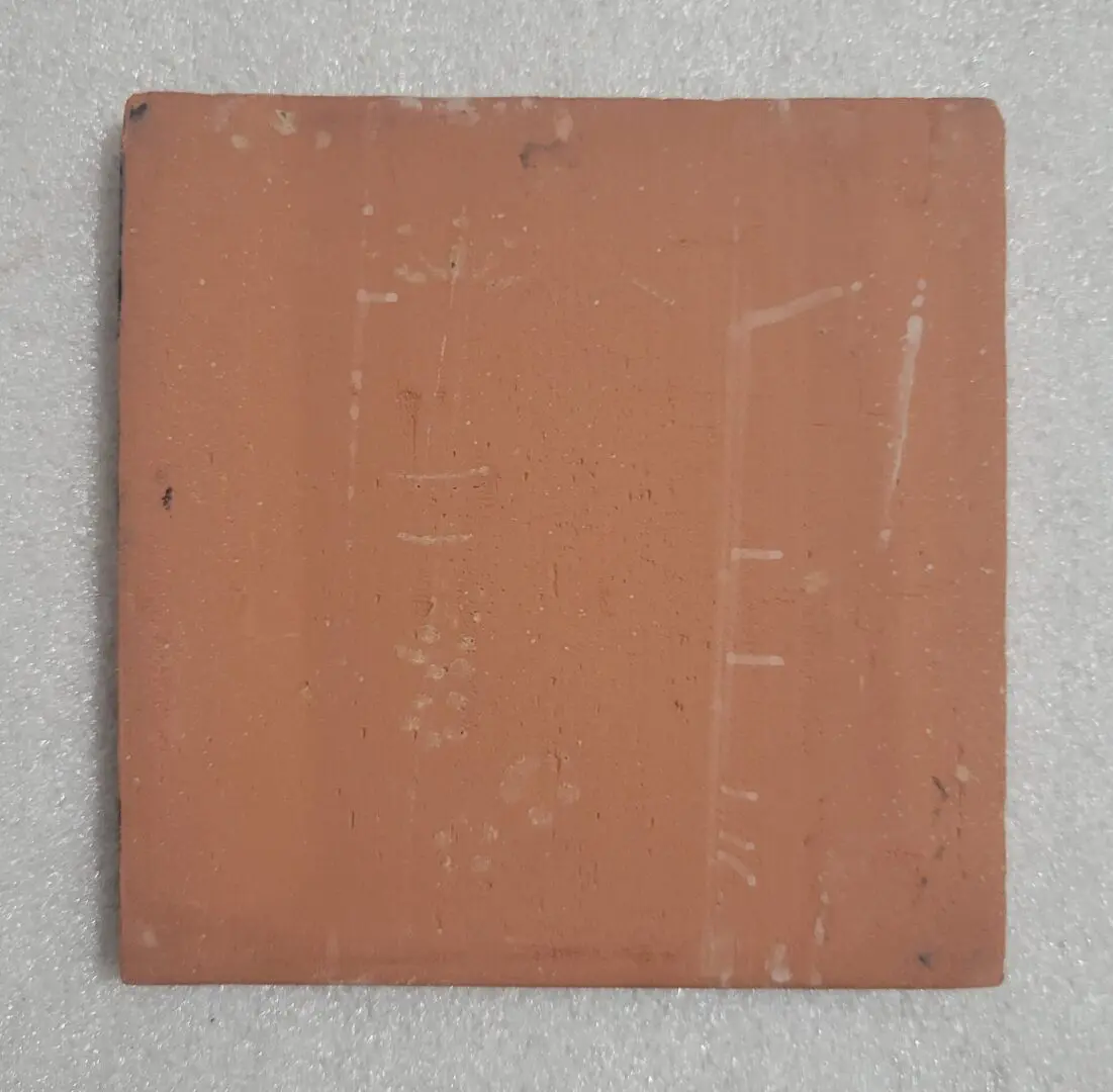A worn, square terracotta tile with surface scratches and marks.