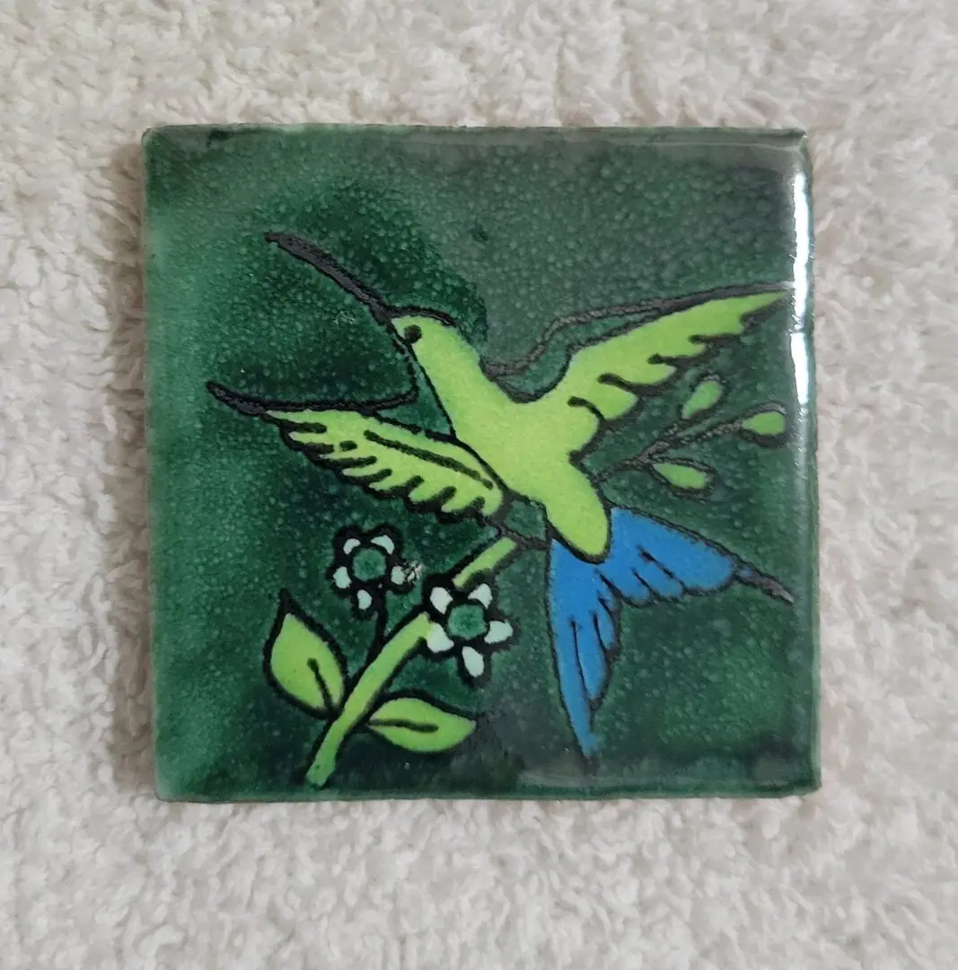 A decorative tile with a hummingbird and flower design.