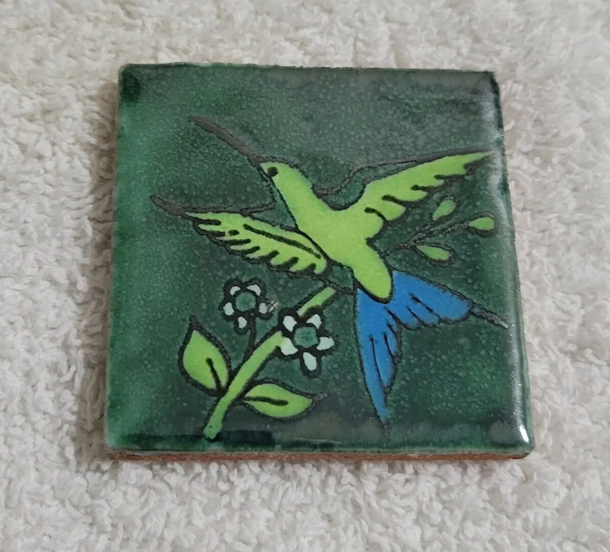 Square tile with a colorful hummingbird and flower design.