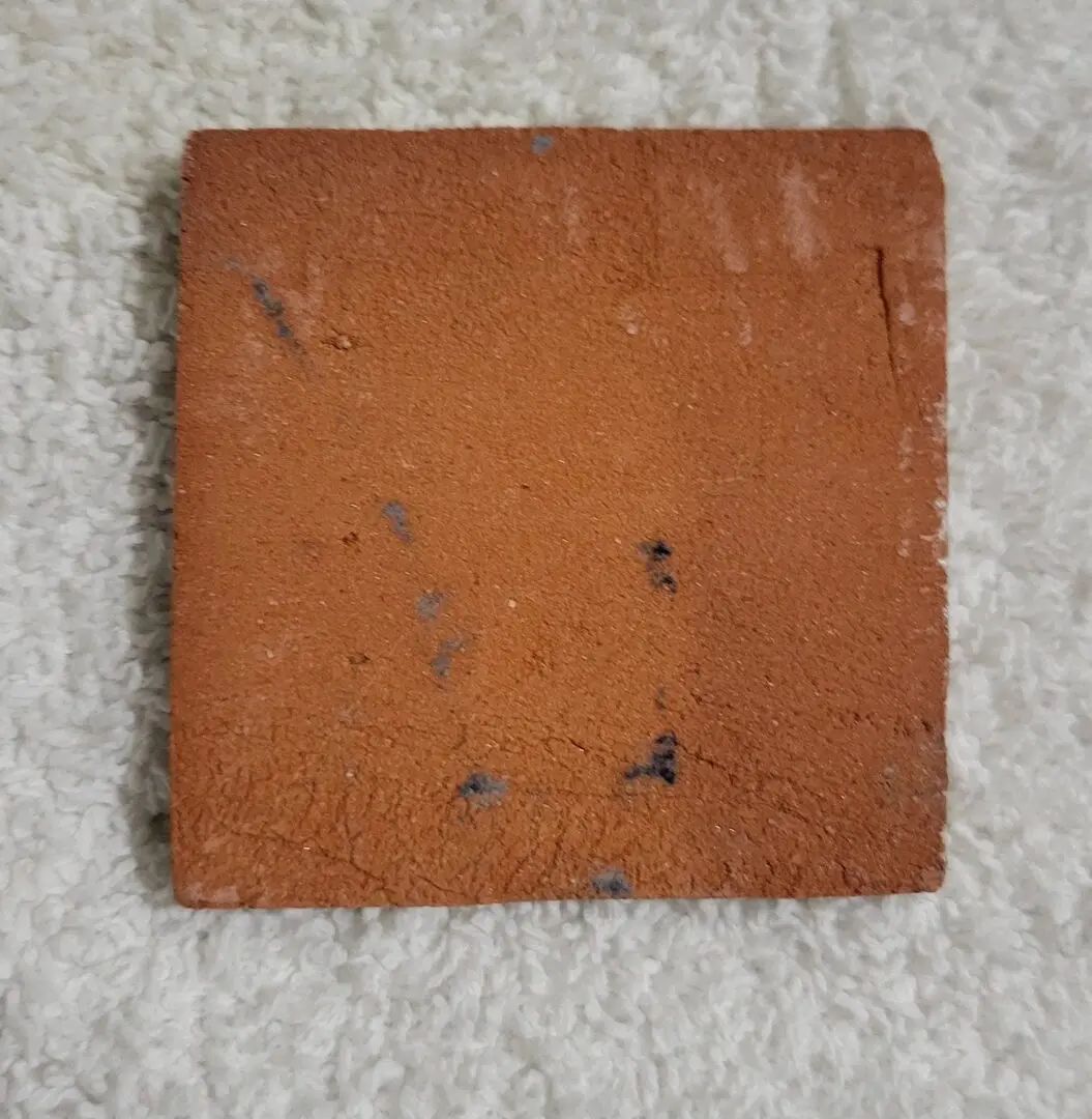 Square brown brick tile on a textured surface.