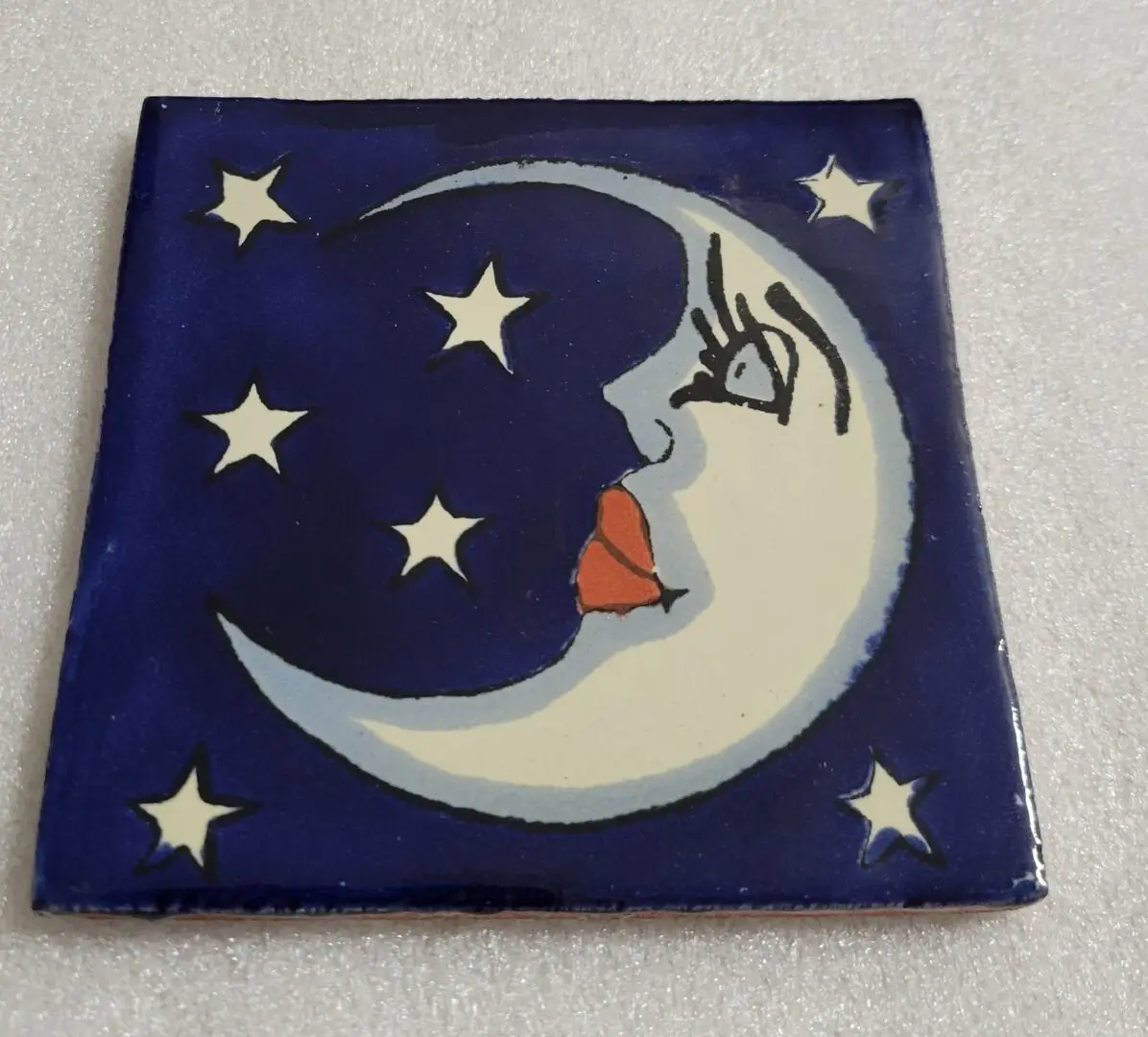 Moon face with stars on blue tile.