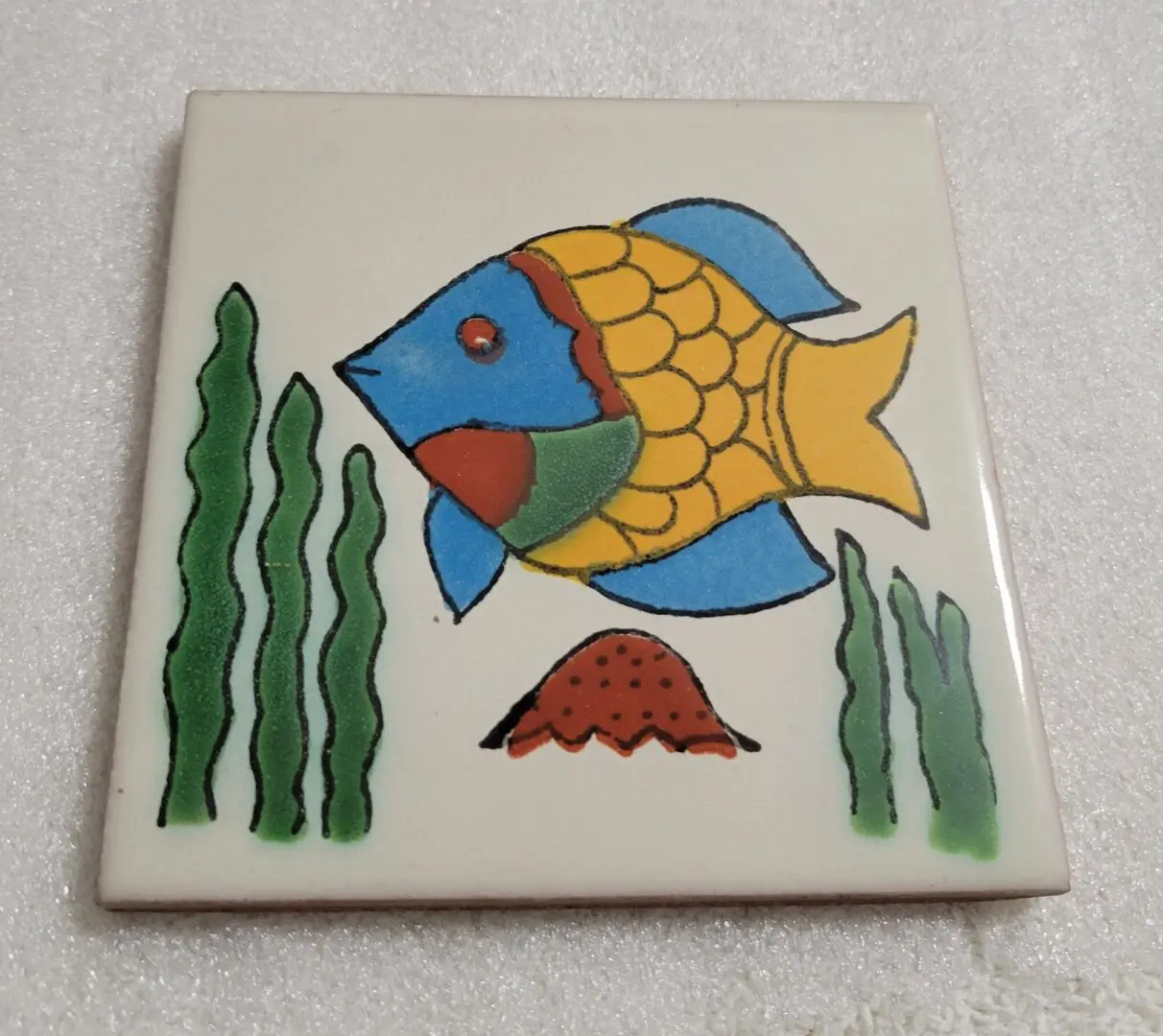Colorful fish on ceramic tile with seaweed.