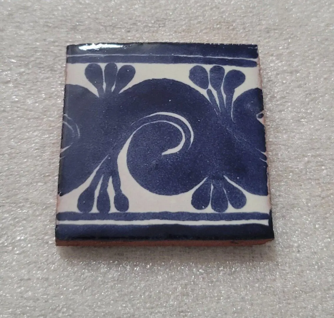 Decorative ceramic tile with blue floral swirl design.