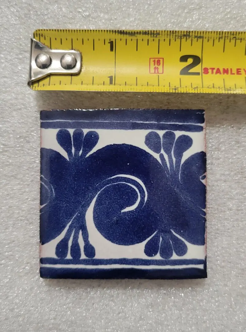 Blue and white ceramic tile with floral design and measurement scale.