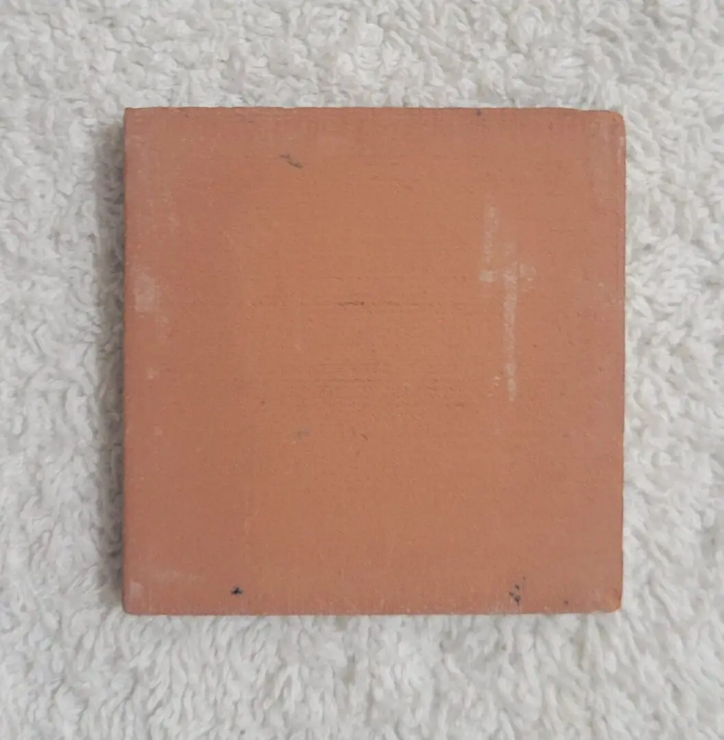 Square terracotta tile on white textured fabric