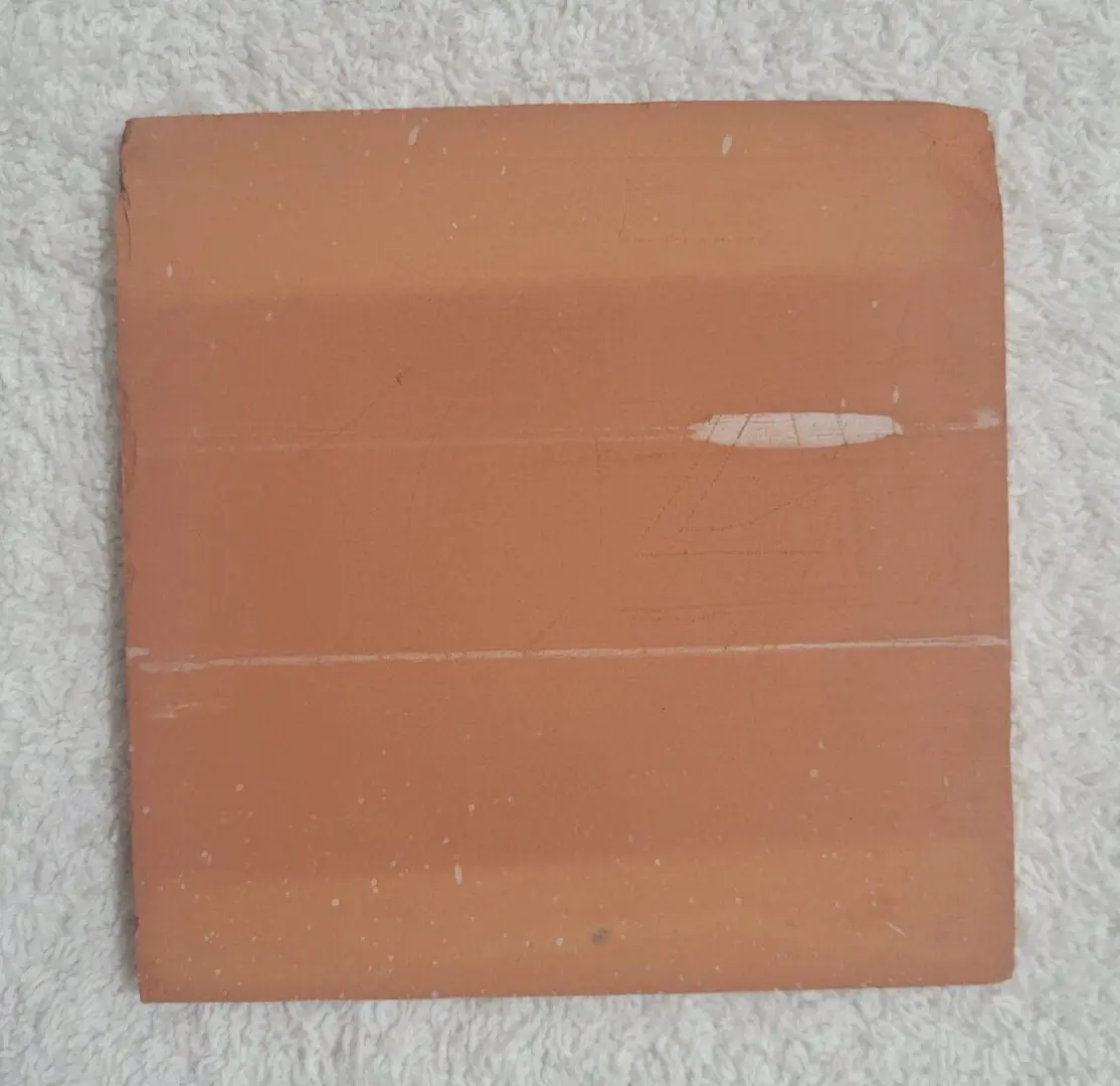 Square terracotta tile on white fabric.