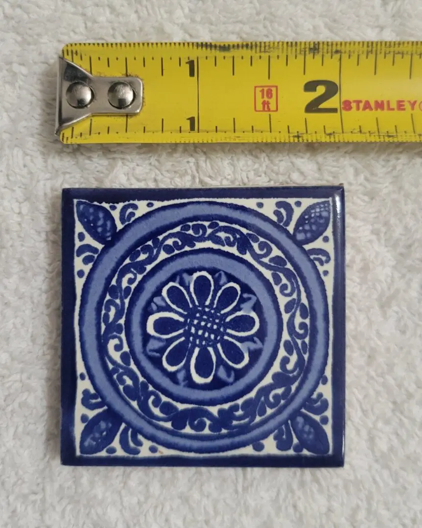 Blue decorative tile with measuring tape above.