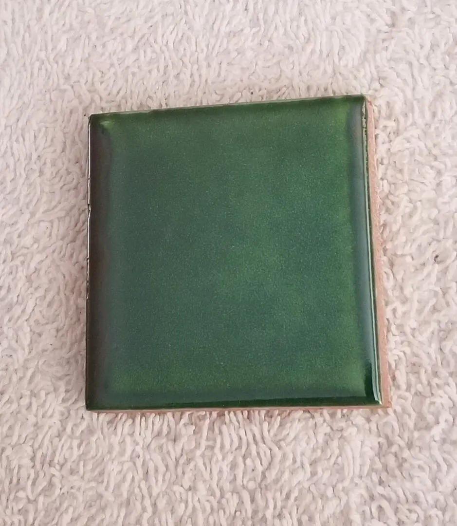 Square green glazed ceramic tile on towel