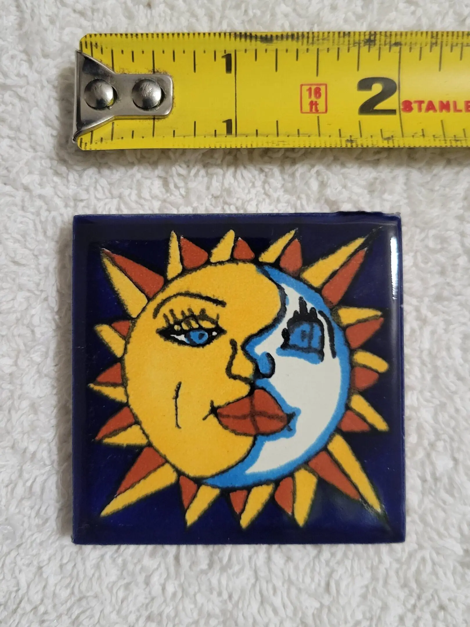 Decorative tile featuring a sun and moon design with a ruler for scale.