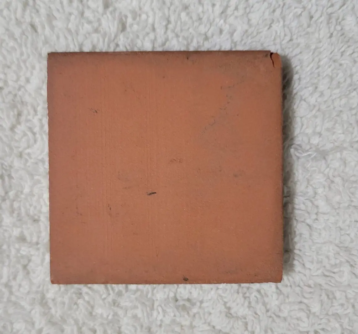 Square terracotta tile on a gray textured surface.