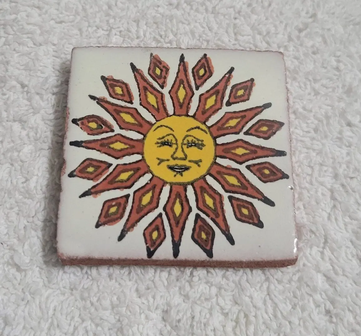 Decorative tile featuring a stylized sun with a face and radiating rays.