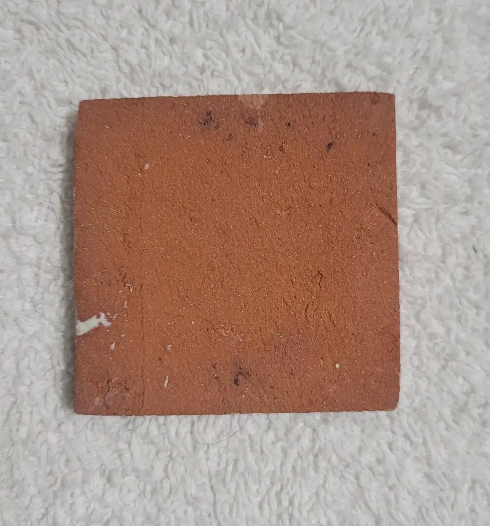 Worn terracotta square tile on white fabric