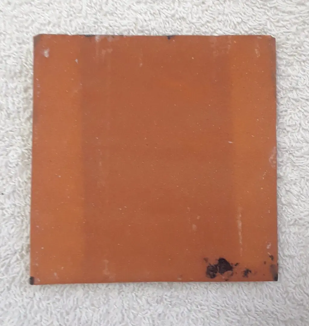 Orange ceramic tile on textured surface.