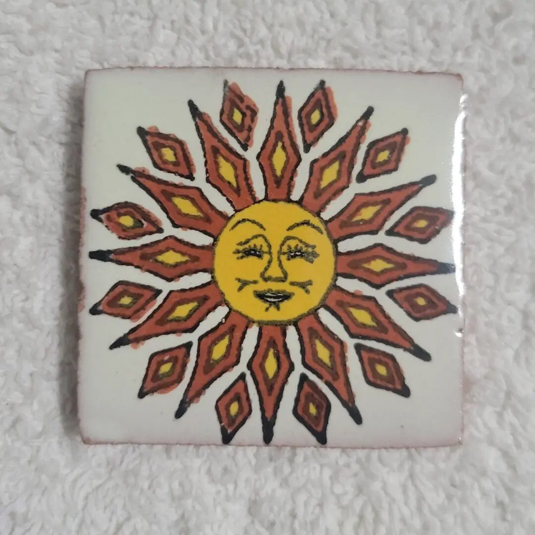 Decorative tile featuring a stylized sun with a face and radiant rays.