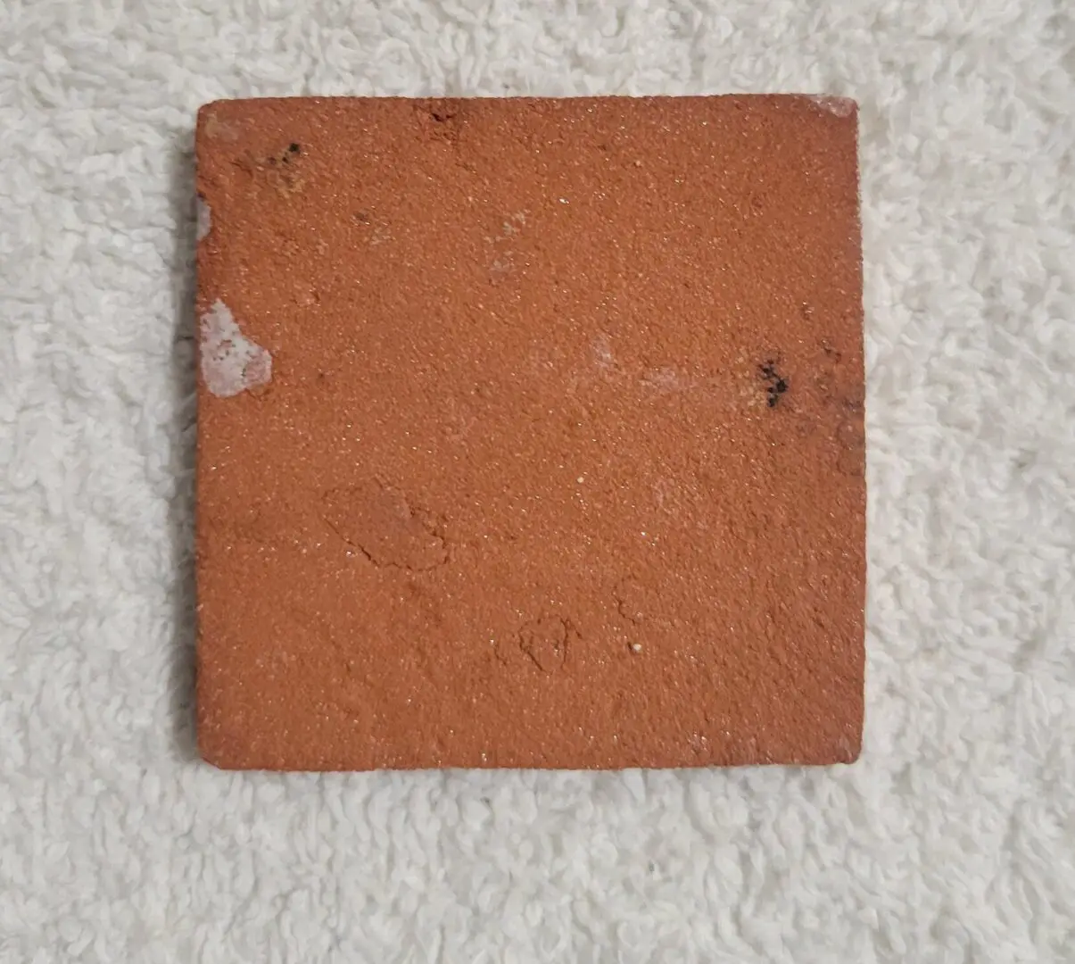 A square orange tile with minor chips on a textured background.