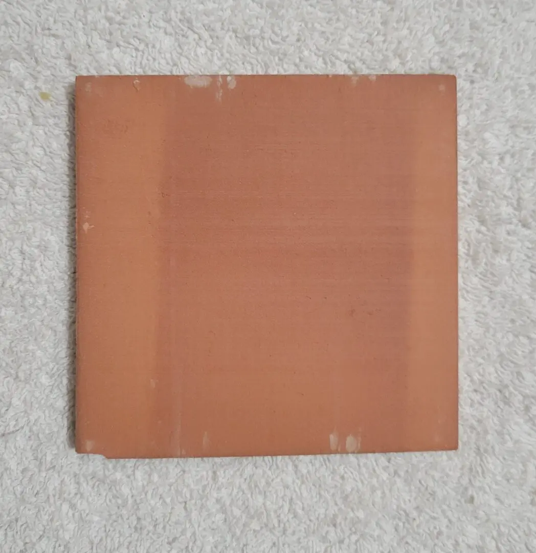 A plain, square, orange book without a visible title on a gray surface.