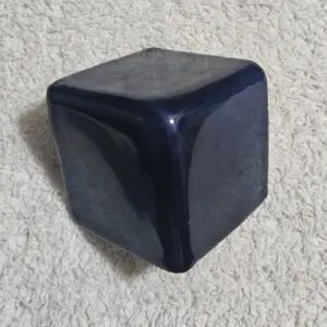Dark, shiny, irregular cube on textured surface.