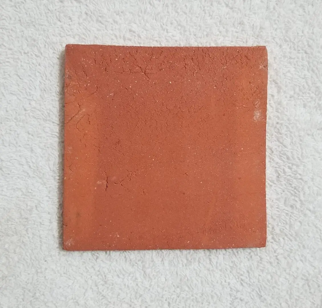 Square terracotta tile with rustic texture on a light surface.