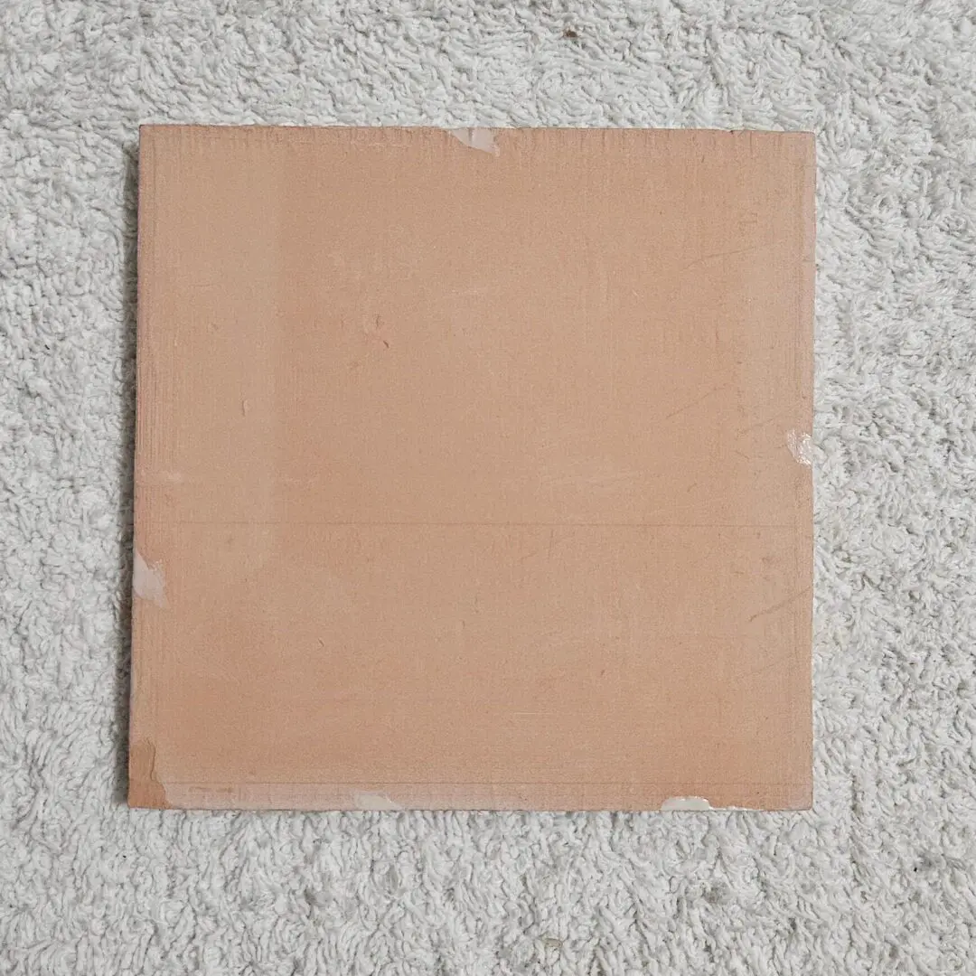 Square beige tile on a textured surface.