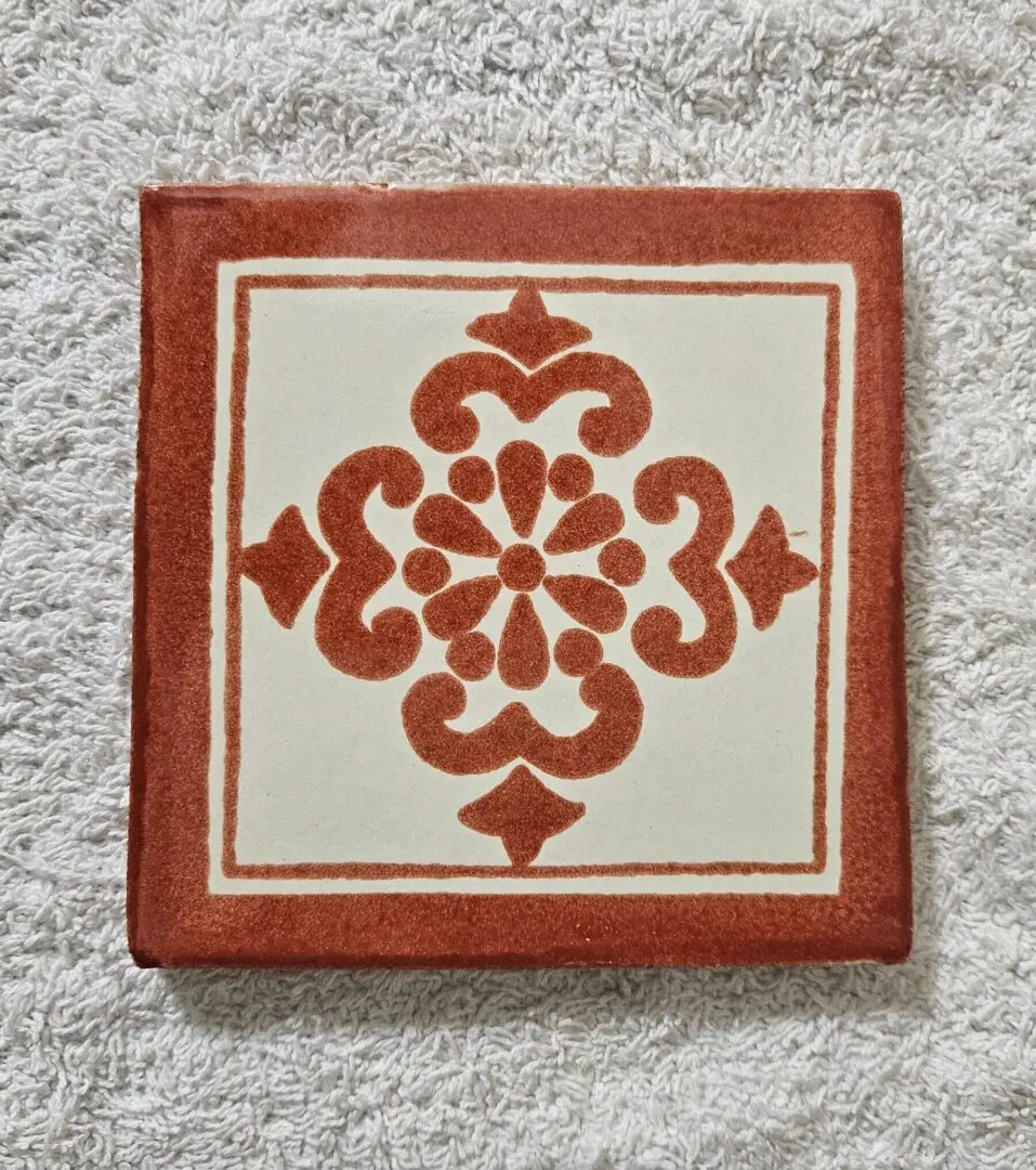 Decorative square tile with a red floral pattern on white.