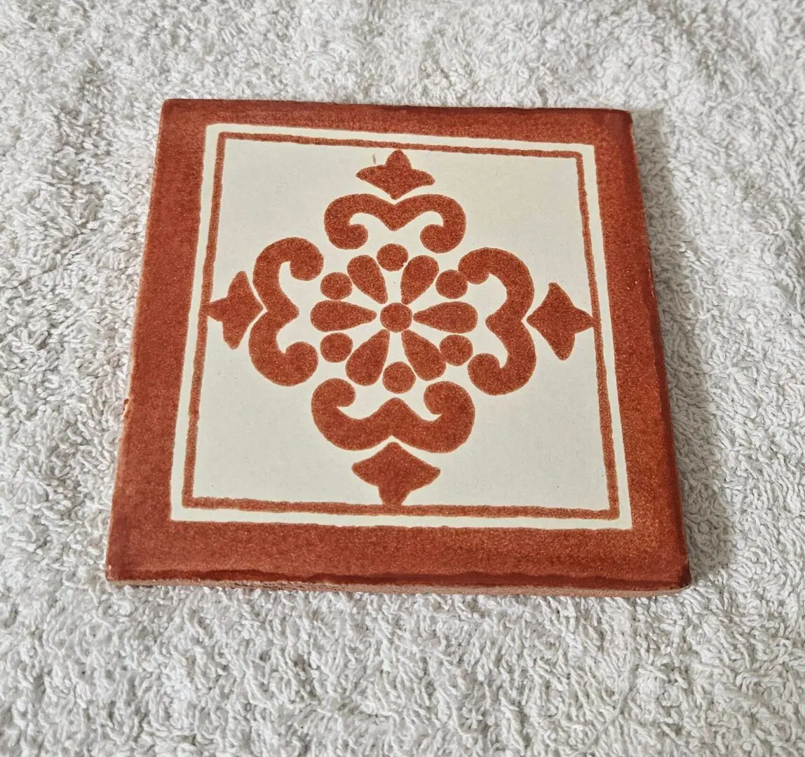 Decorative ceramic tile with red floral pattern on white background.