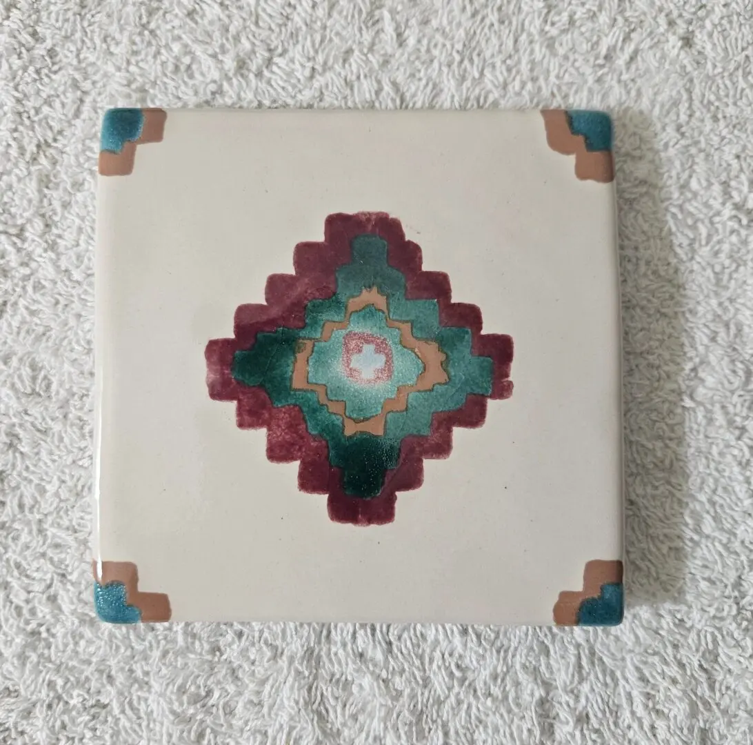 Decorative ceramic tile with geometric pattern and corner accents.