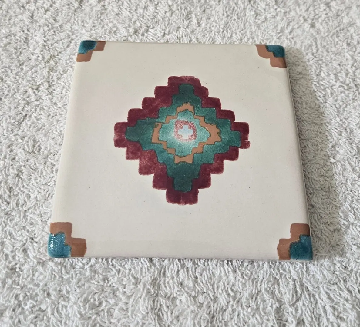 Decorative square tile with a colorful geometric pattern and corner accents.