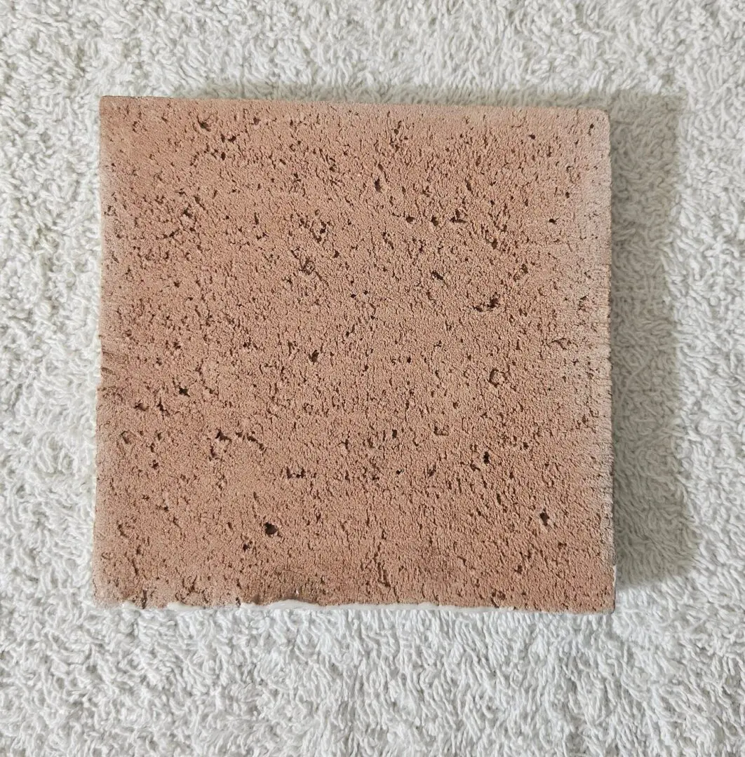 A textured, square brown tile on a white surface.