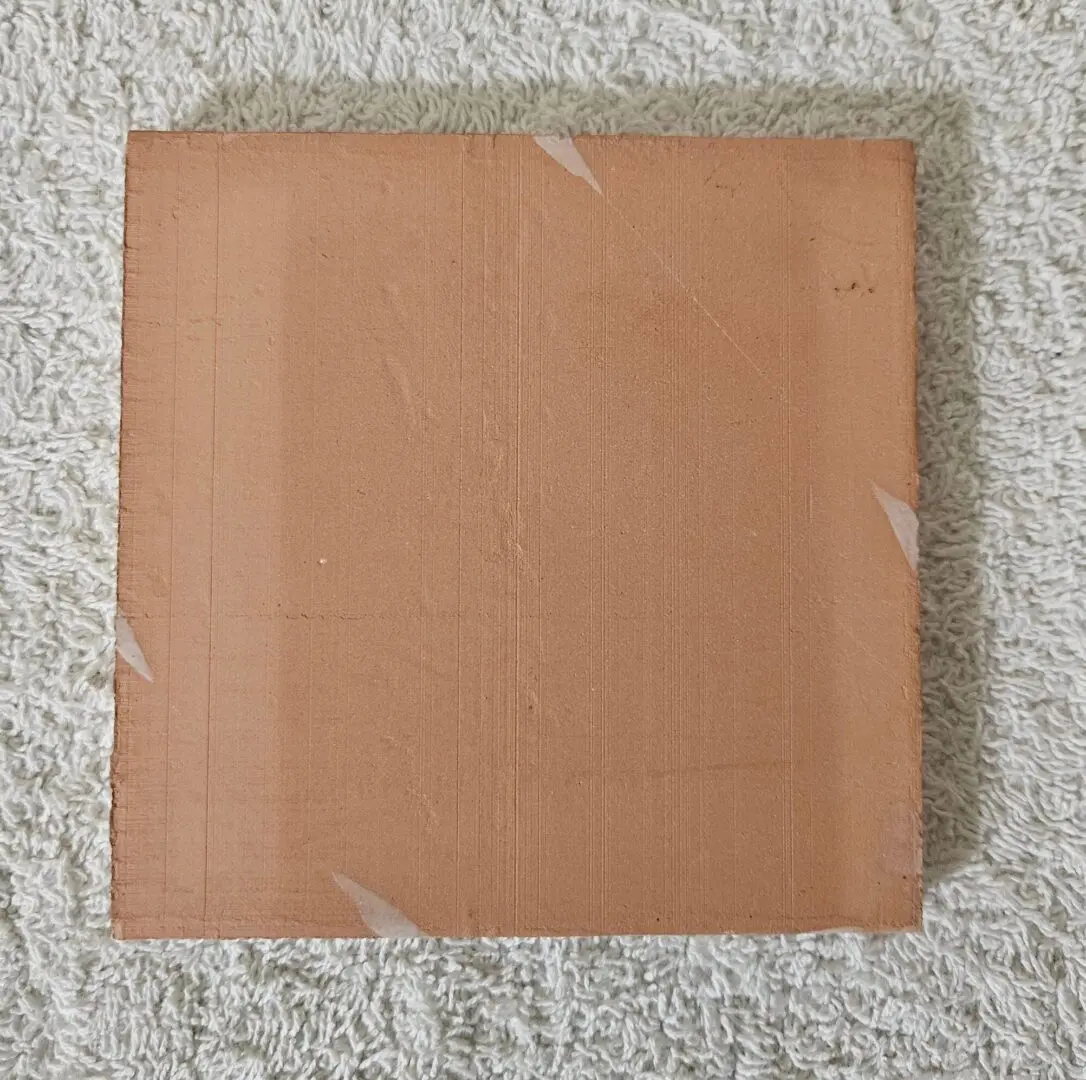 Square piece of brown cardboard on a textured surface.