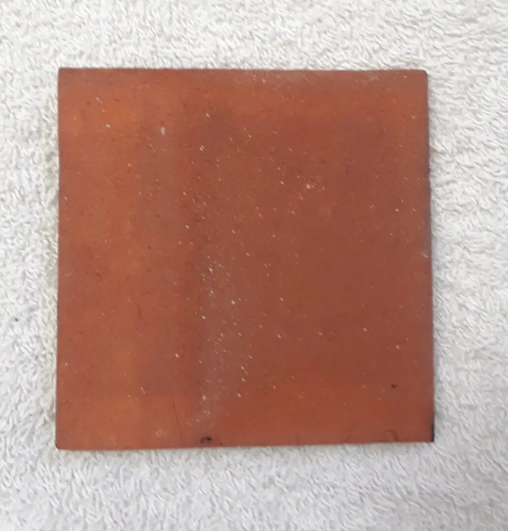 A square reddish-brown ceramic tile on a light surface.