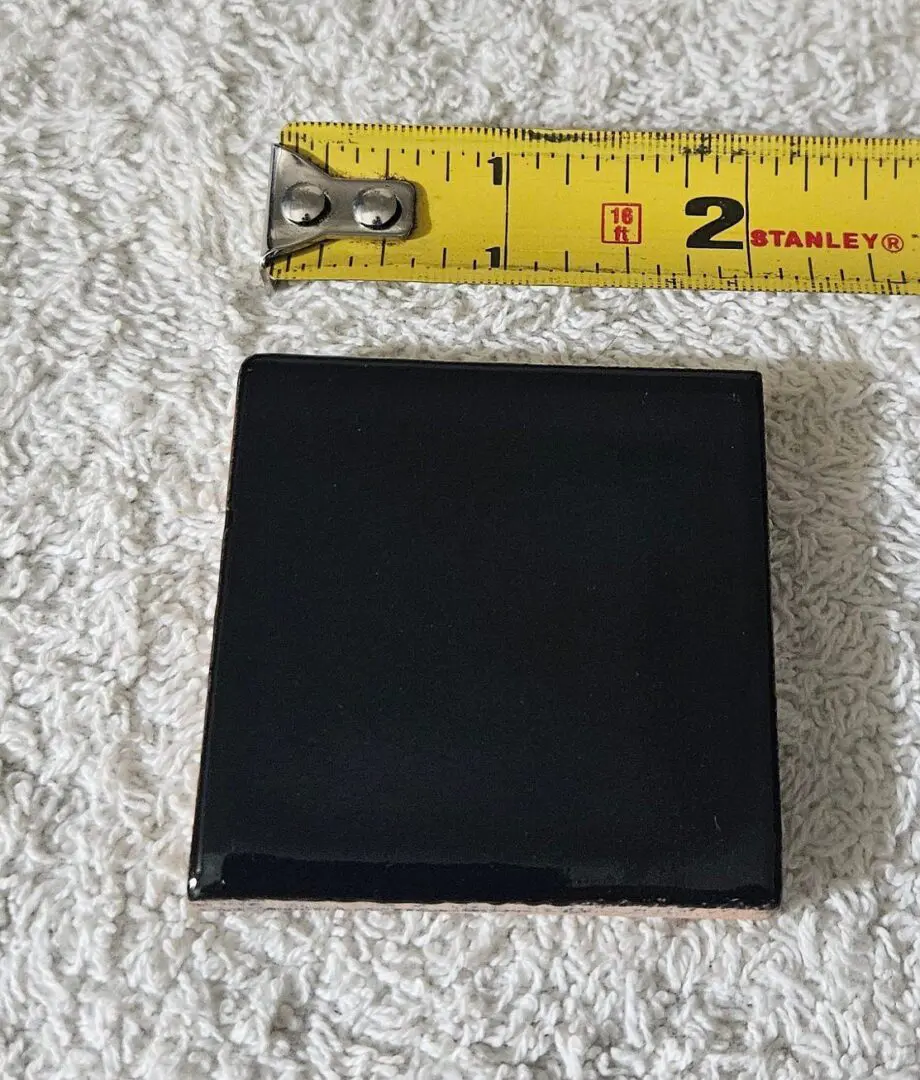 Black wallet placed on a textured white surface next to a measuring tape showing about 3 inches.