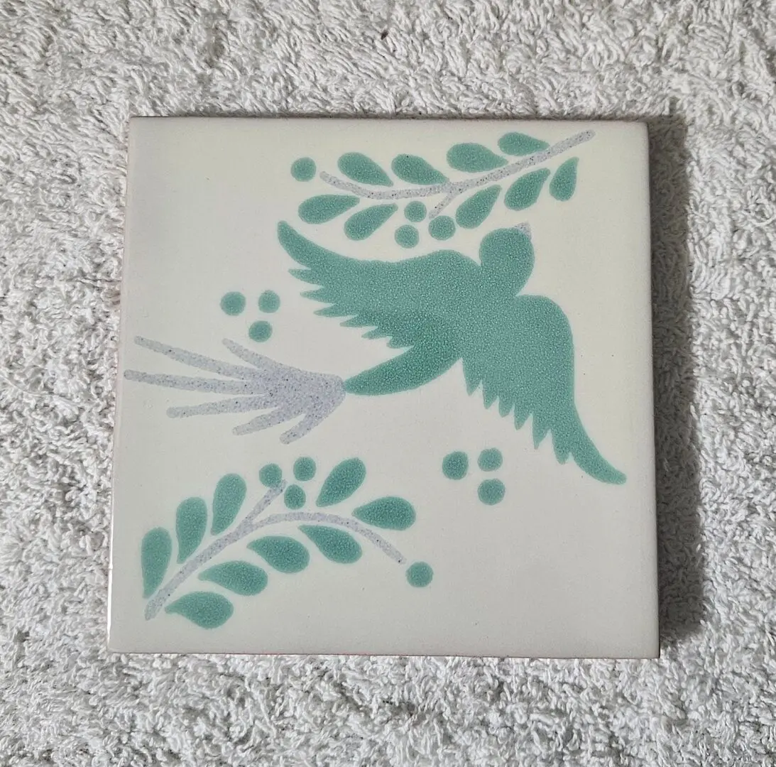 A decorative ceramic tile with a teal bird and foliage design.