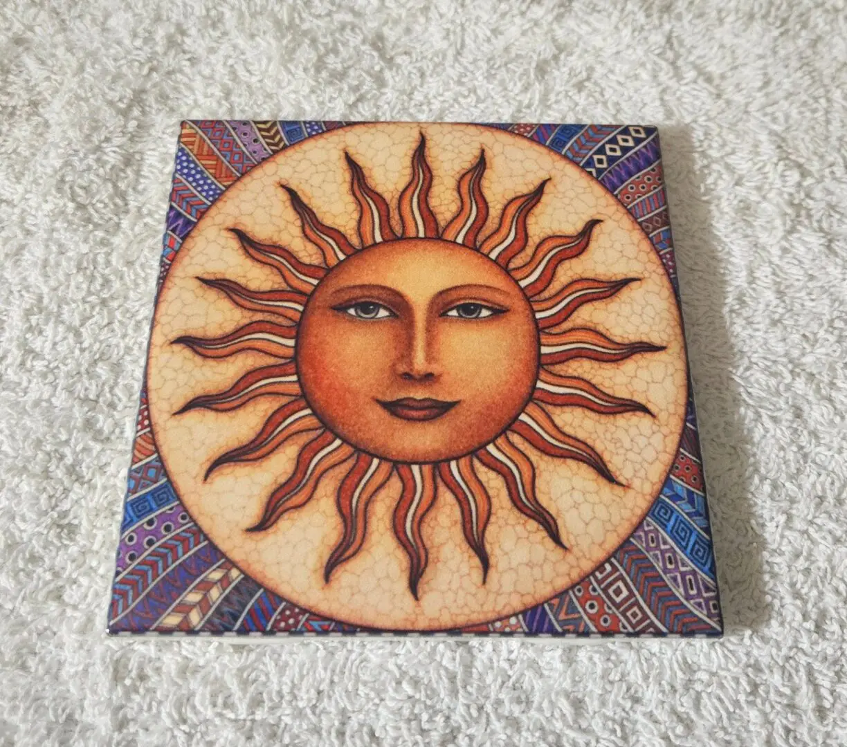Sun face artwork on colorful patterned tile.