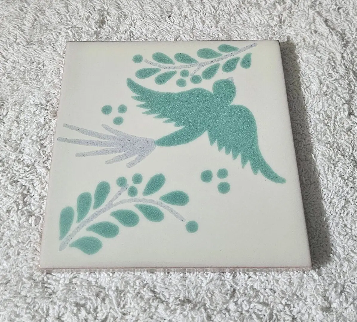 Decorative ceramic tile with a teal bird and leaf design.