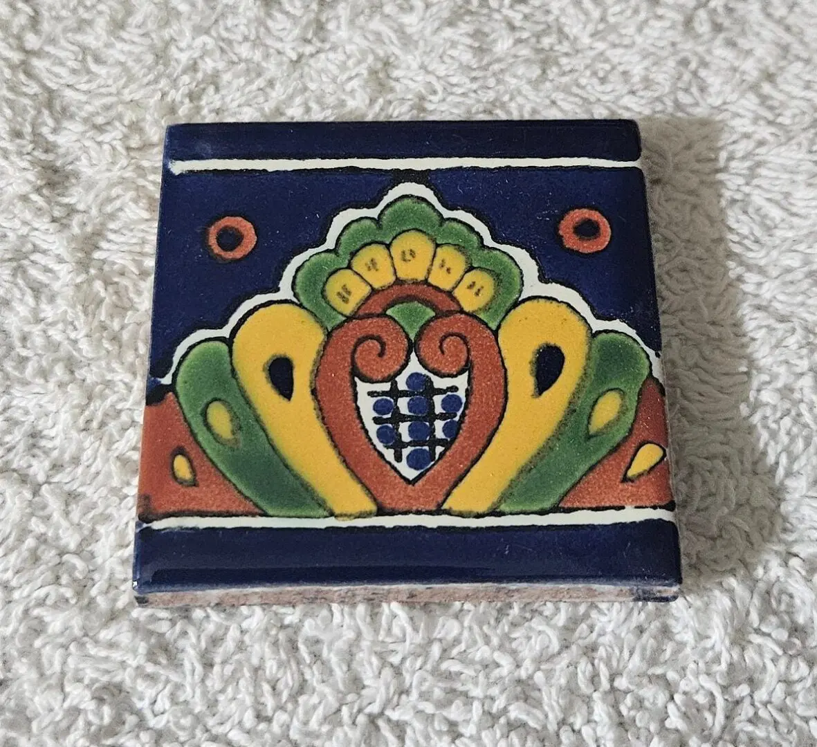 Decorative ceramic tile with colorful peacock motif on navy background.
