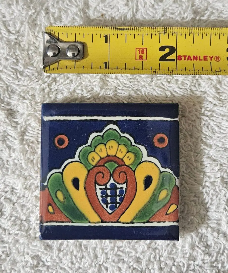 Colorful ceramic tile with heart and floral design beside measuring tape.