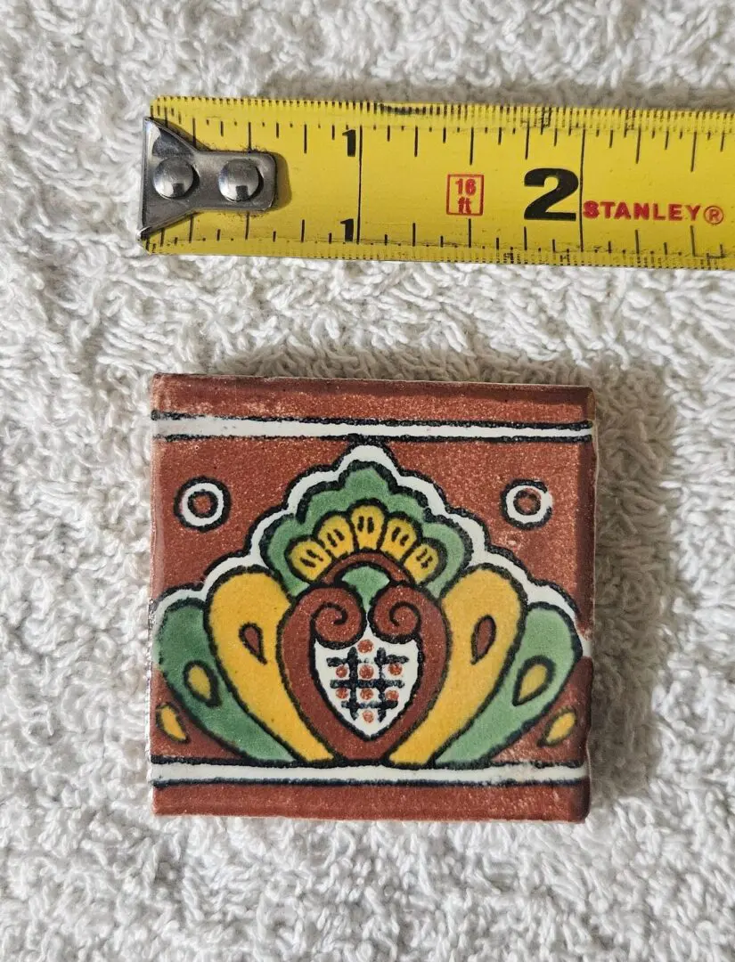 Ornate patterned ceramic tile beside measuring tape