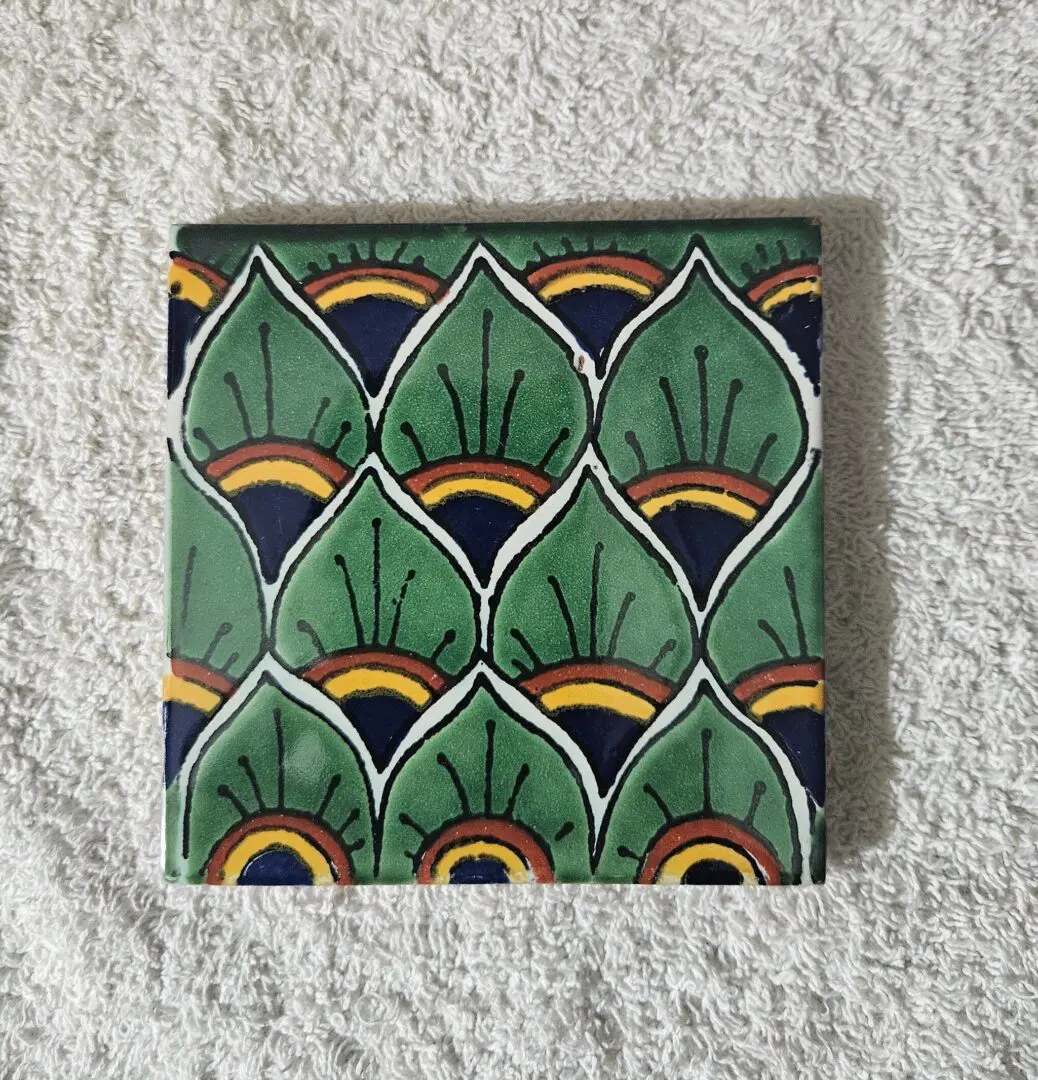 Square tile with green, black, and yellow abstract leaf pattern.