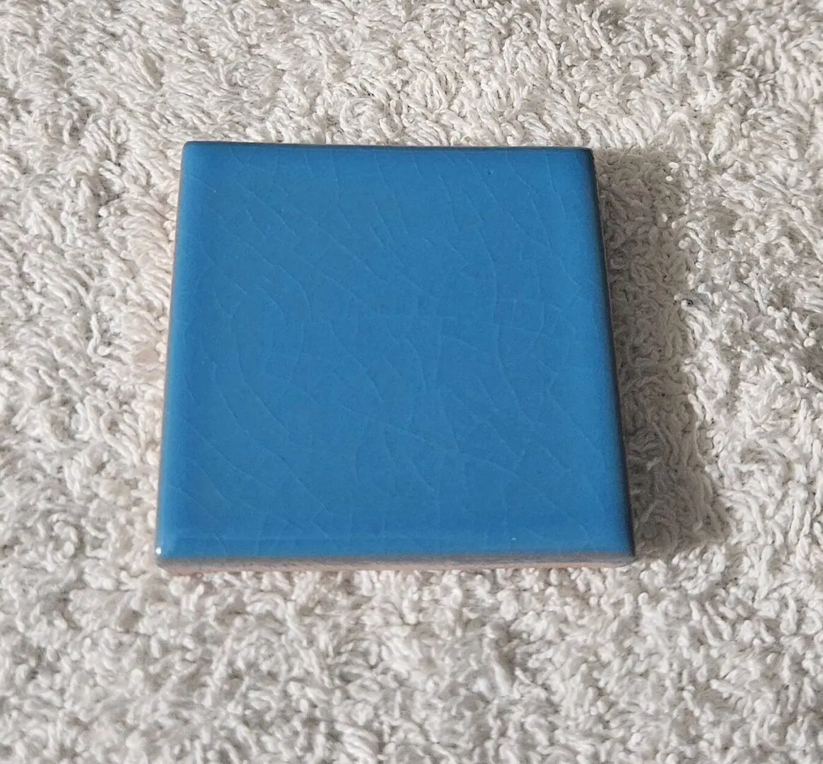 A blue square tile on a textured surface.