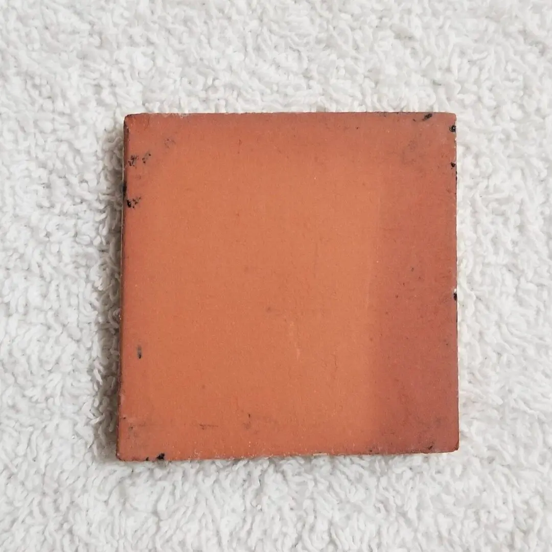 A single square terracotta tile on a textured white surface.
