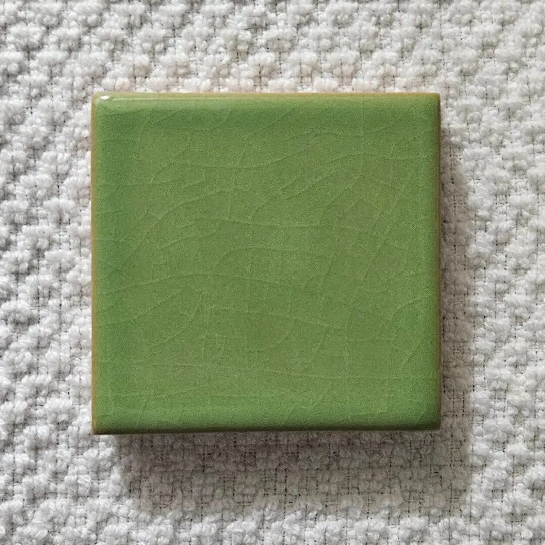Green square ceramic tile on textured fabric surface.