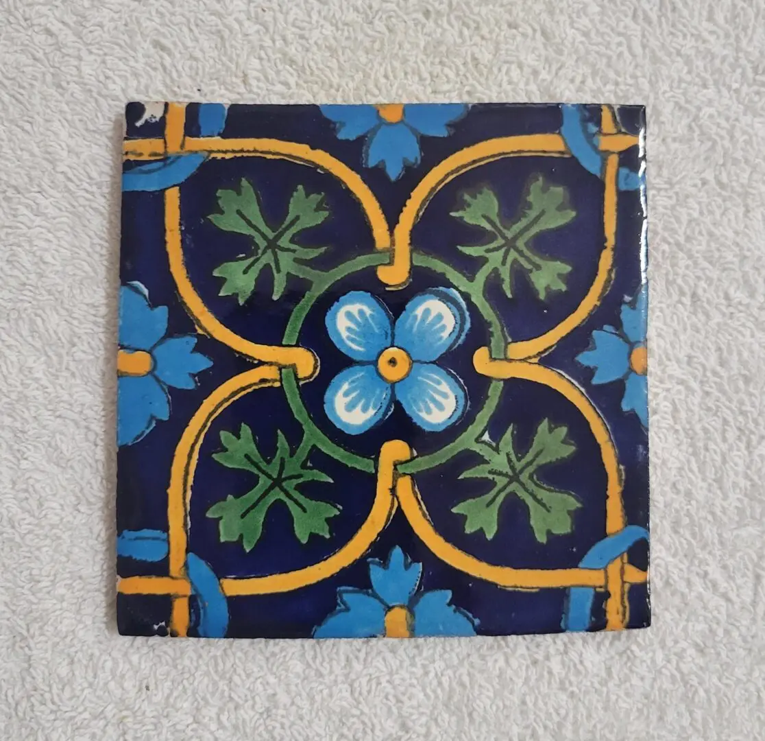 Square ceramic tile with floral and vine patterns in blue, green, and yellow.