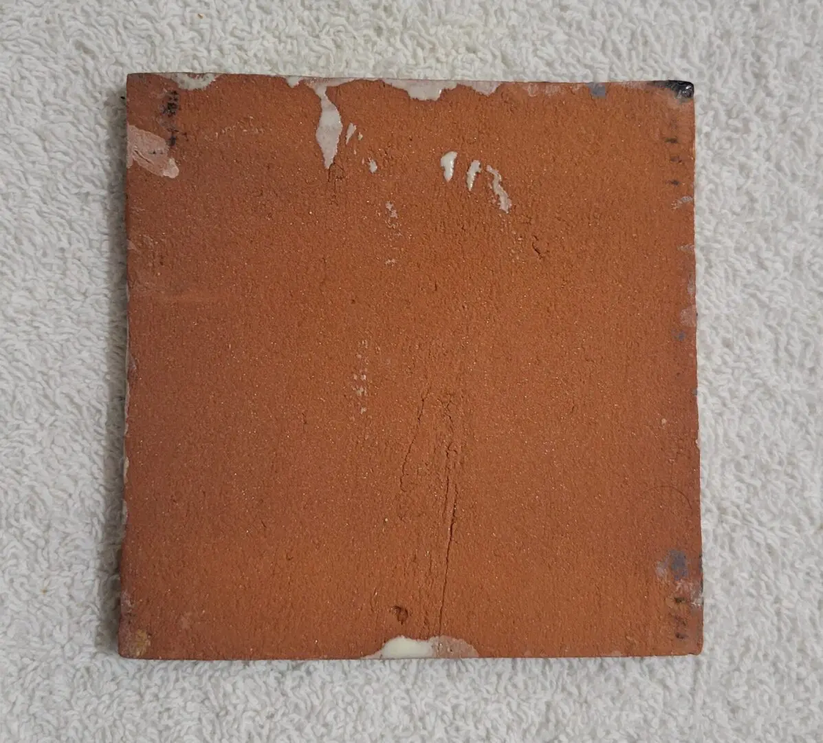 A worn, square terracotta tile with chipped edges.