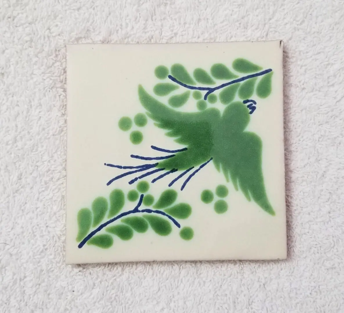 Decorative tile with a green hummingbird and leafy branches.